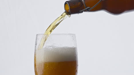 closeup bottle pouring beer into glass at white background. lager drink flowing