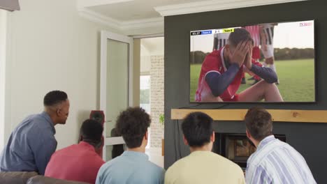 video of diverse friends sitting on sofa and watching football on television at home