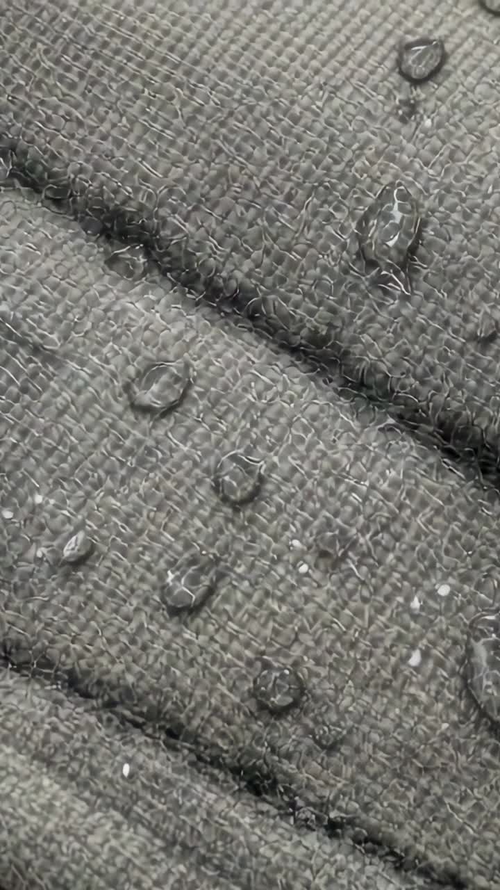 Vertical video: Cam panning drops beading, merging on seam, lint sticking as fabric repelling water