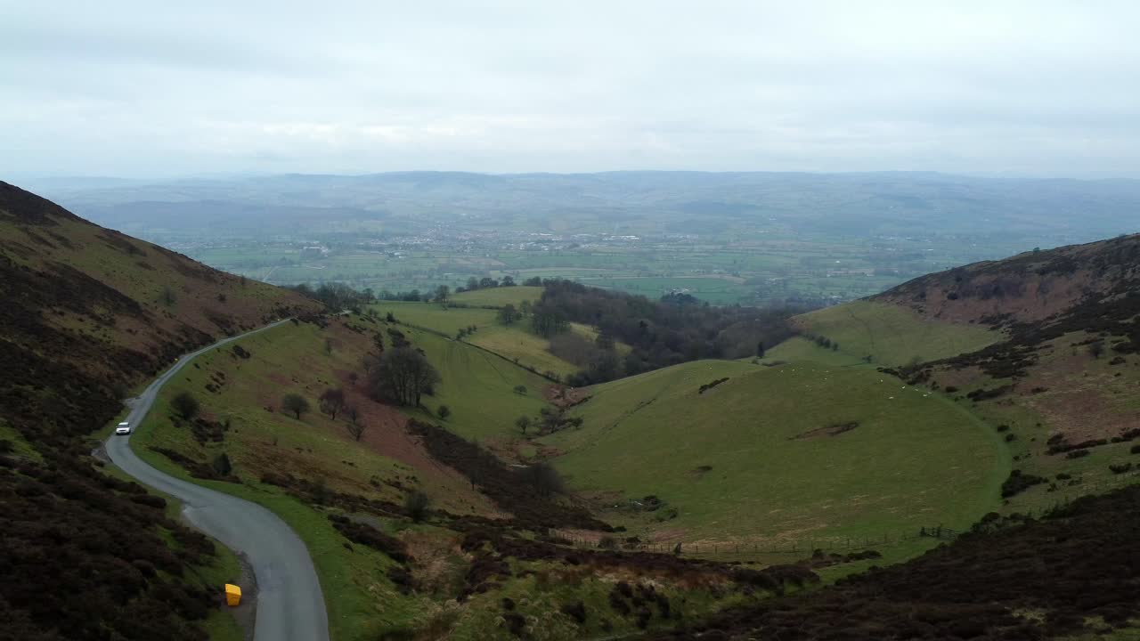 vehículo blanco que conduce un camino rural único y estrecho que atraviesa el paisaje de valles de montaña verde galés