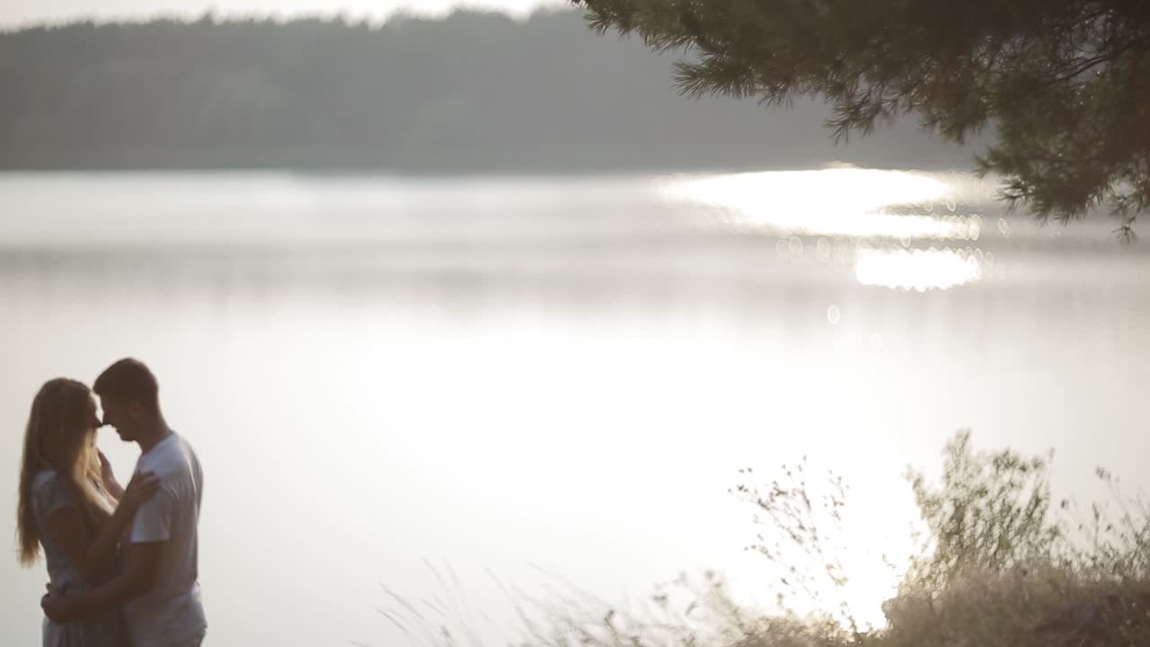 Young Couple Walk To River Bank. Young couple in love holding hands watching sunrise together outdoors by the lake