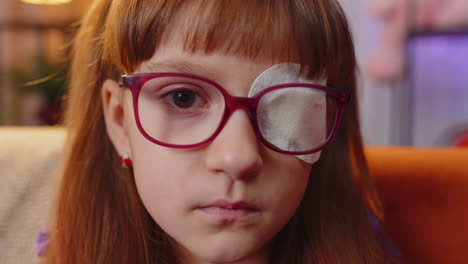 Sick ill toddler girl looking at camera having protective bandage plaster patch scratch on one eye