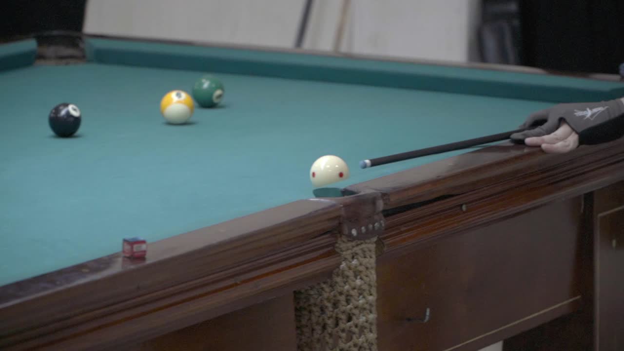 Een speler schiet en slaat een bal in een hoekzak tijdens een potje pool.