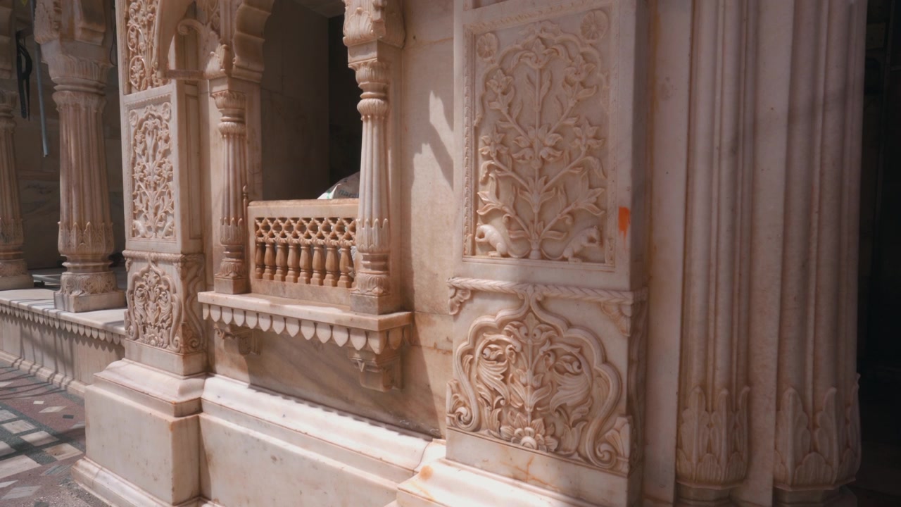 Ripresa cinematografica statica in primo piano di intagli floreali decorati e rilievi architettonici su pareti di marmo bianco all'interno del tempio di Karni Mata nel Rajasthan, India