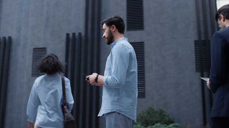 Uomo attraente che manda messaggi in una vivace zona centrale. Persone d'affari che passano.