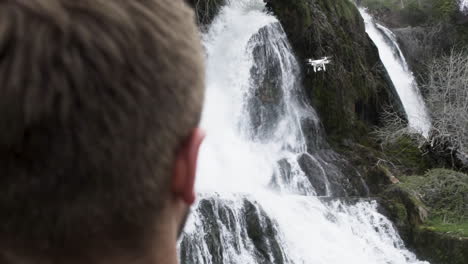 young creative watching his drone in front of waterfall