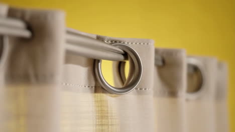close-up of curtains with grommets on a rod against a yellow wall