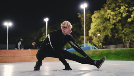 Sportive-Blond-Man-Stretching-Legs-Before-Training-In-The-Park-At-Night-2