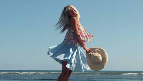 attractive blonde holding straw hat spinning on beach