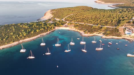 Aerial-drone-footage-flying-towards-boats-and-catamarans-anchored-in-a-small-bay-at-sunrise,-next-to-Rukavac-on-the-Island-of-Vis-in-Croatia