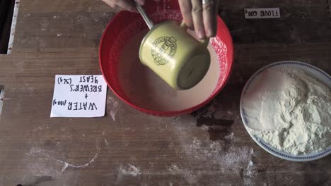 woman mix water and brewer for bread cake recipe over the wood with labeled ingredient