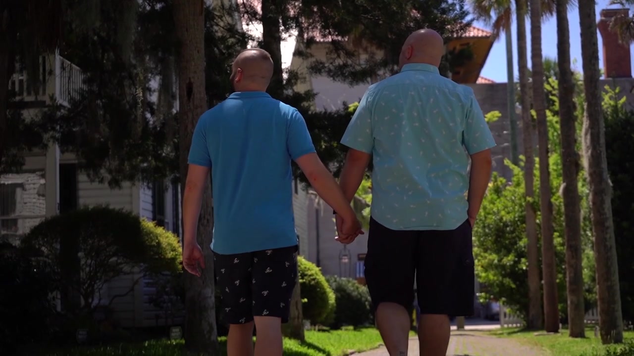 Pareja gay tomados de la mano paseando por una calle lateral de vacaciones.
