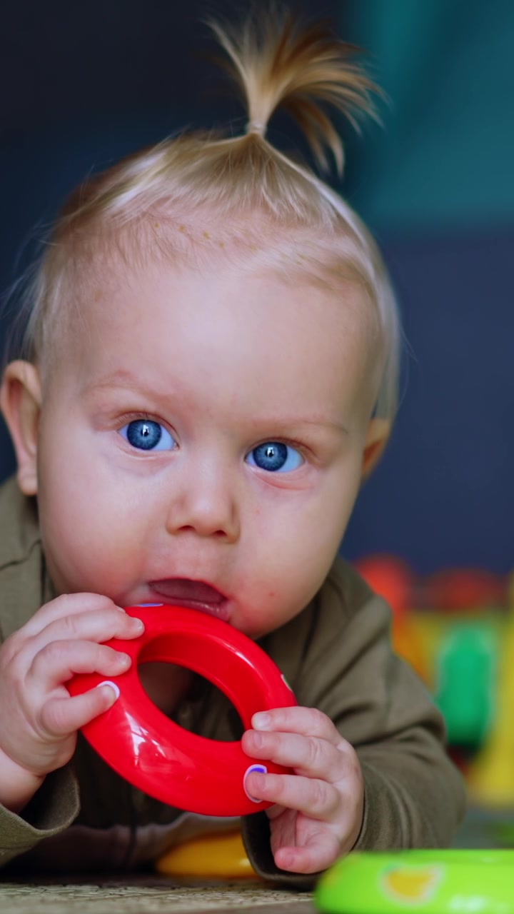 Adorable chubby infant lies on the floor on belly. Lovely baby chews the toy, looks up and smiles. Close up. Vertical video