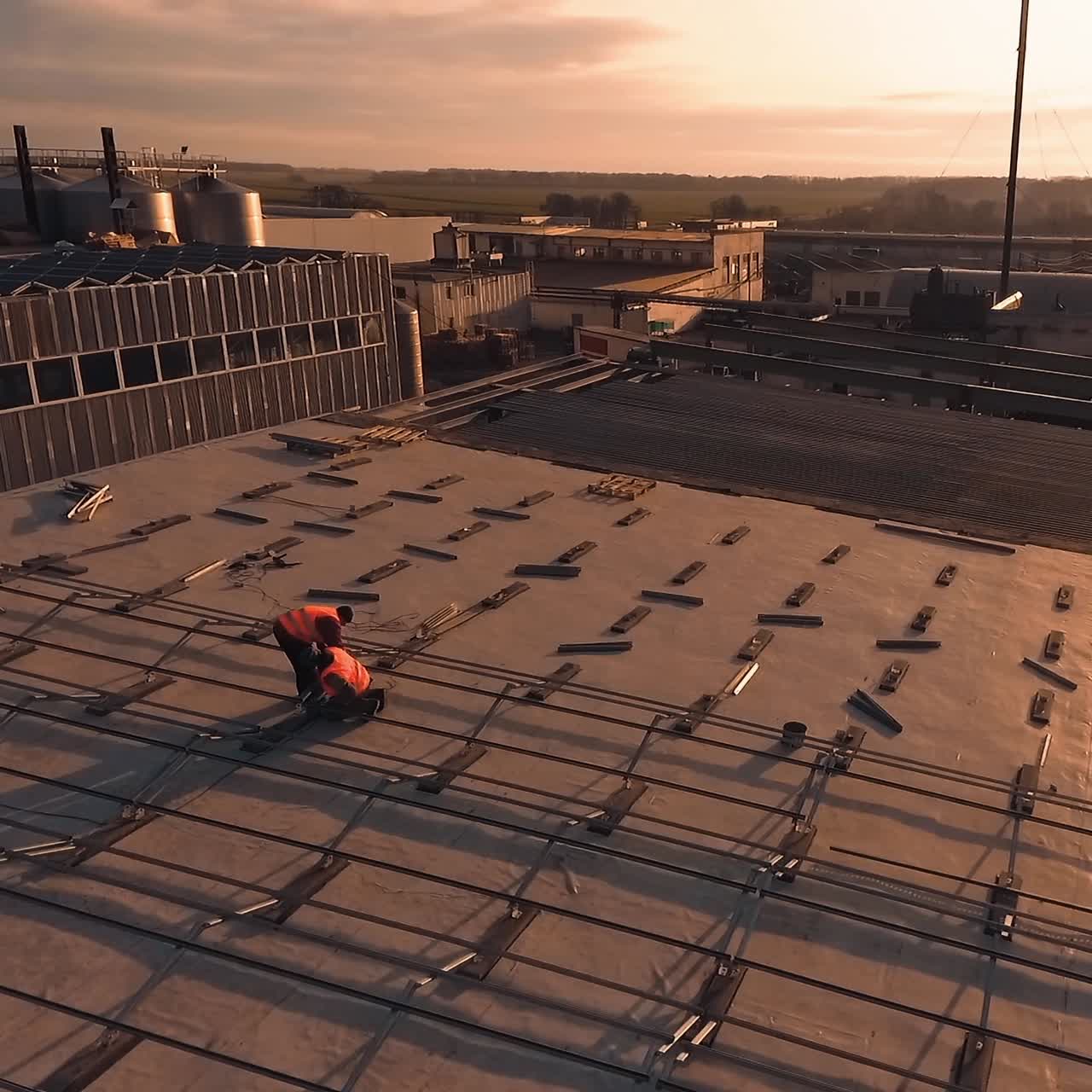 Construction of solar farm on roof of a building. Workers install metal constructions for solar panels at sunset. Aerial view.