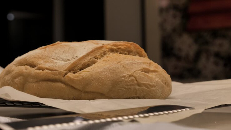 Slow pan around freshly baked loaf of sour dough bread topped with flour sitting on kitchen bench with tea towel and tray, low depth of field