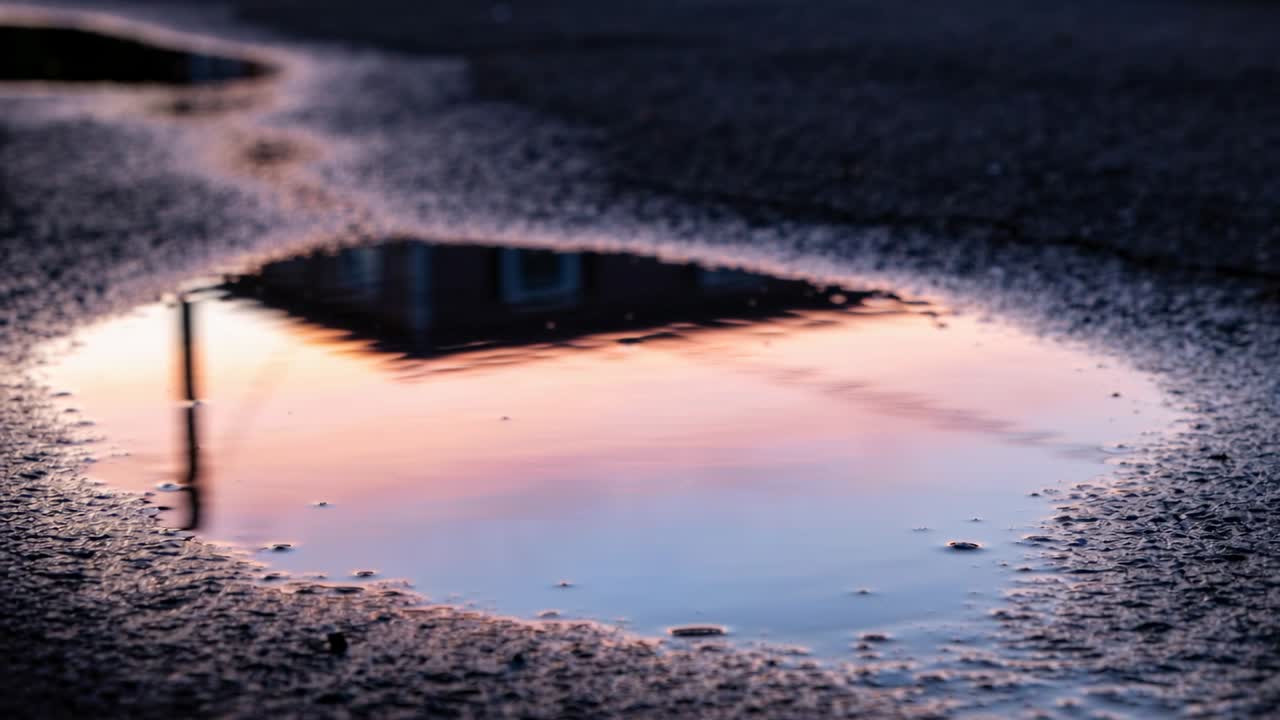 雨上がりの道路の浅い水たまりが切妻屋根とポールを映し出し、水滴が波紋を広げている。