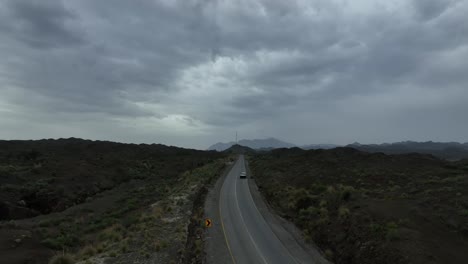 Toma-Aérea-De-Un-Dron-De-Una-Carretera-Con-Un-Vehículo-Moviéndose-Por-La-Carretera-Y-Un-Paisaje-Perdido-Y-Nubes-Oscuras-En-El-Cielo