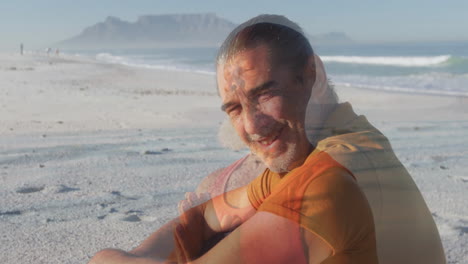 sitting on sandy beach, man smiling with ocean and mountain in background