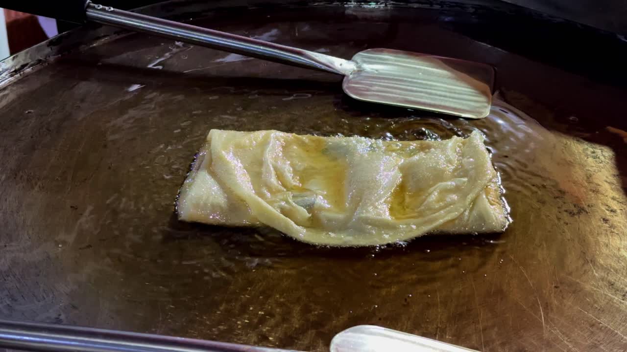 la masa de huevo martabak o "martabak telur" se rocía con aceite caliente sobre fuego bajo