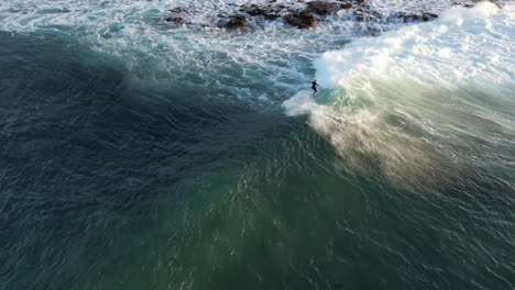 High-aerial-view-of-a-surfer-riding-a-white-foaming-wave-near-the-Australian-coastline