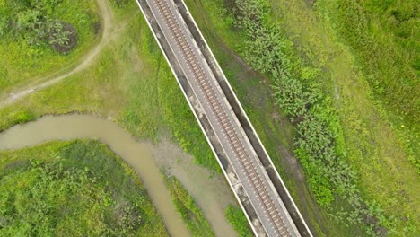 descending aerial footage revealing dirt roads, canal filled with rain water in this marshy land, elevated railway