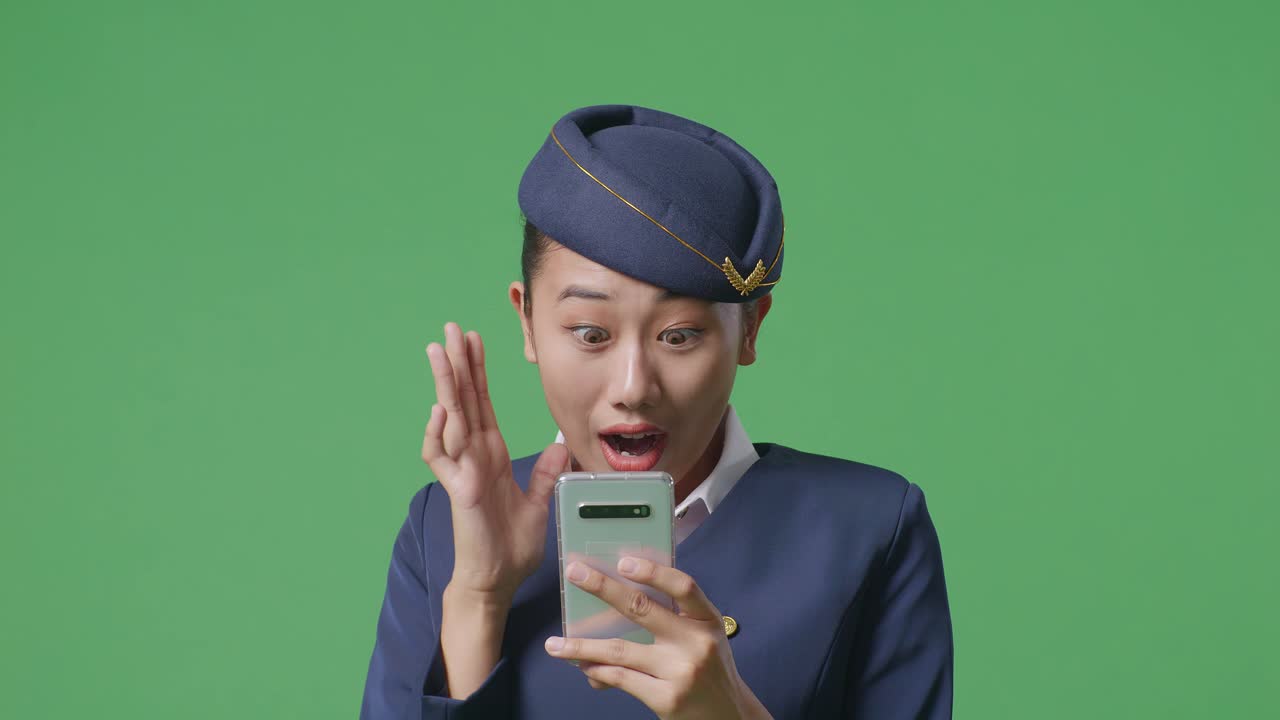 아시아 여성 승무원이 스마트폰을 보고 미소 짓고 초록색 스크린 배경 스튜디오에 서서 와우라고 말합니다.