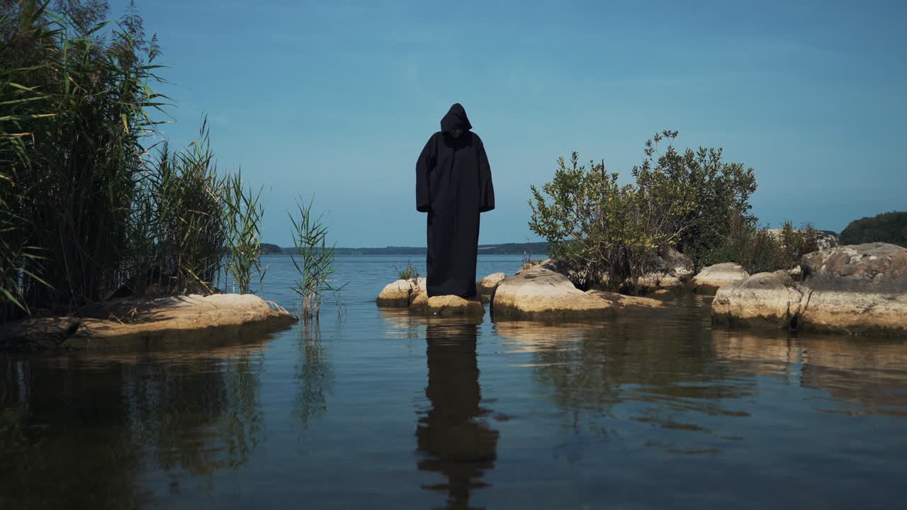 Terrible demon standing in the river. Scary figure in black mantle.