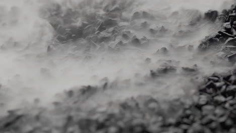 close-up macro shot of mist rising through black stones and covering the screen