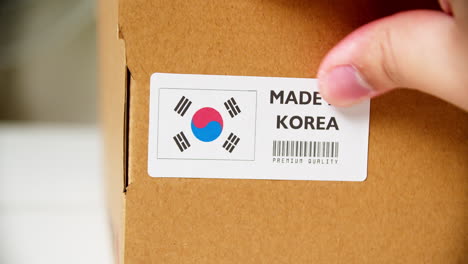 hands applying made in korea flag label on a shipping cardboard box with products