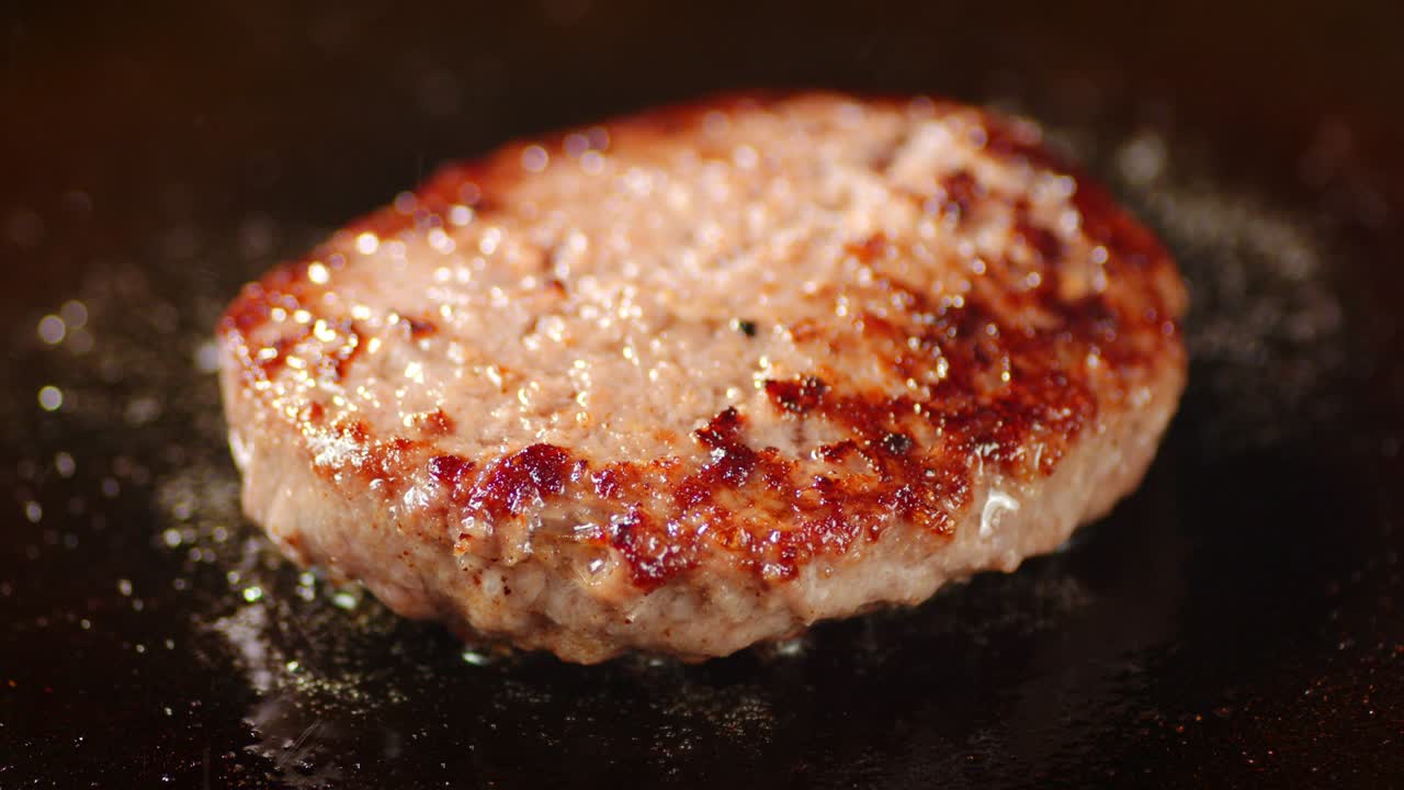 Fried burger in a frying pan with splashes of hot oil.