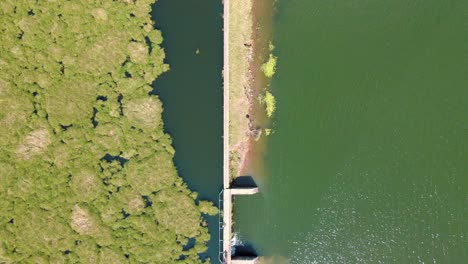 Vogelperspektive-Auf-Den-Fluss-Mit-Damm-Und-Brücke,-Während-Kinder-An-Einem-Sonnigen-Tag-Darauf-Spielen