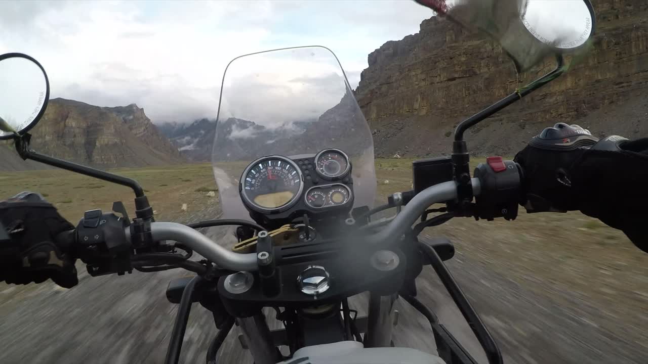 Driving at speed with a motorbike through the Himalayan mountains with grey skies and arid landscapes.