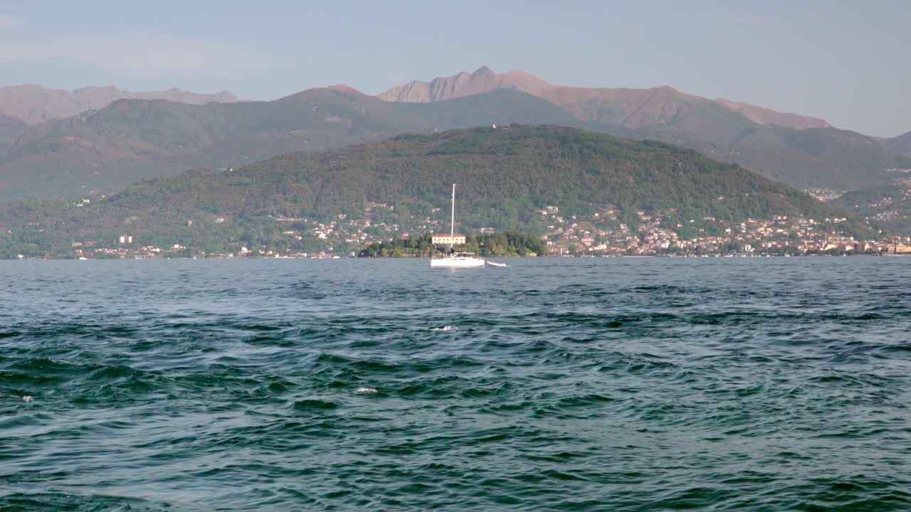 A sailing boat with retracted sails moves across Lake Maggiore