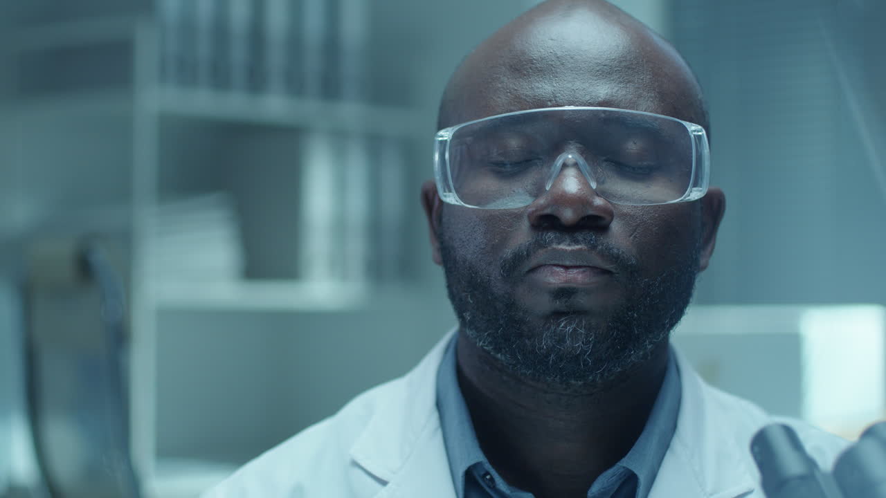 Portrait of African American Lab Scientist in Safety Glasses with Microscope