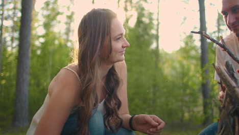 a smiling woman and man together in the woods collect and set up campfire sticks at sunset during a family camping trip