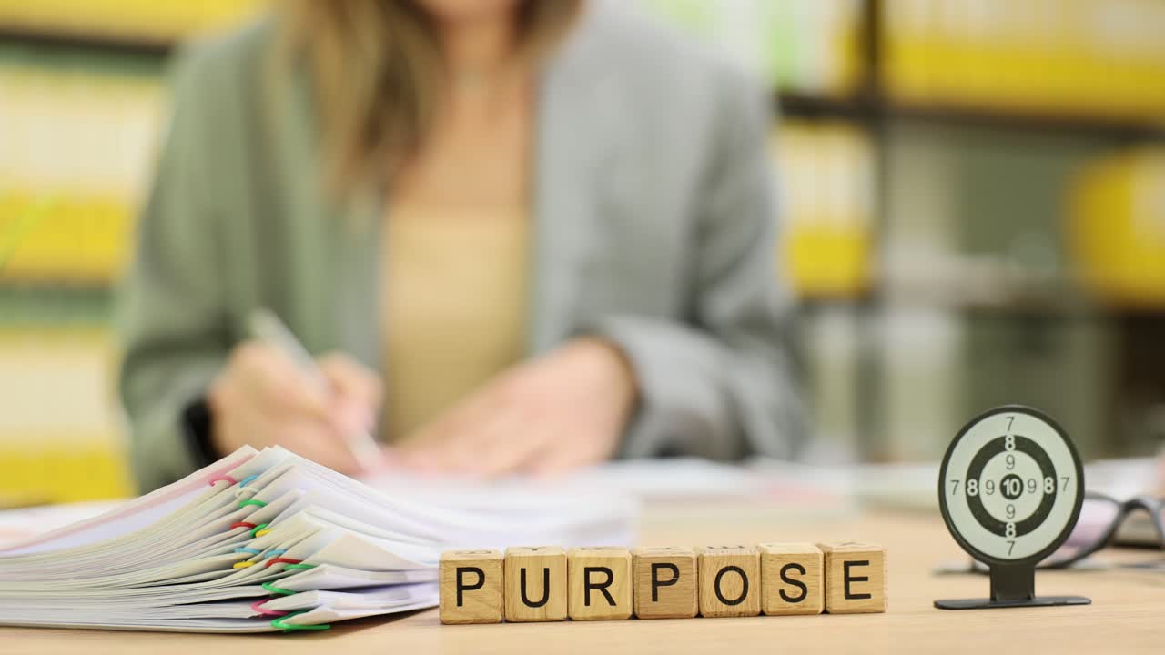 Woman working at a desk with 'PURPOSE' blocks and a target, symbolizing focus and goals