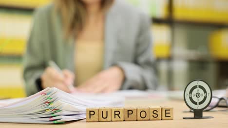 woman working at a desk with 'purpose' blocks and a target, symbolizing focus and goals