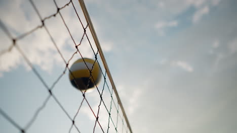 close-up of volleyball net with ball being played over it under open sky, showcasing action during a volleyball game outdoors with clear sky and bright sunlight