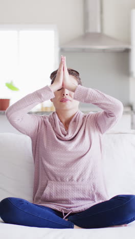 vertical video of happy caucasian woman sitting on couch and meditating