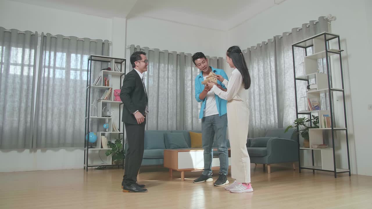 판매용 집에 서 있는 동안 부동산 에이전트로부터 집 모델을 받는 아시아 커플의 전체 시각