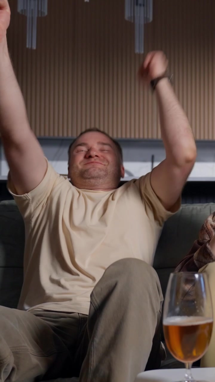 Uomo entusiasta che guarda la TV e festeggia con birra e snack.