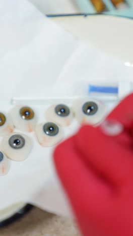 few eye prosthesis in medical bowl. medical specialist in red gloves painting artificial eye in the laboratory. close-up. vertical video