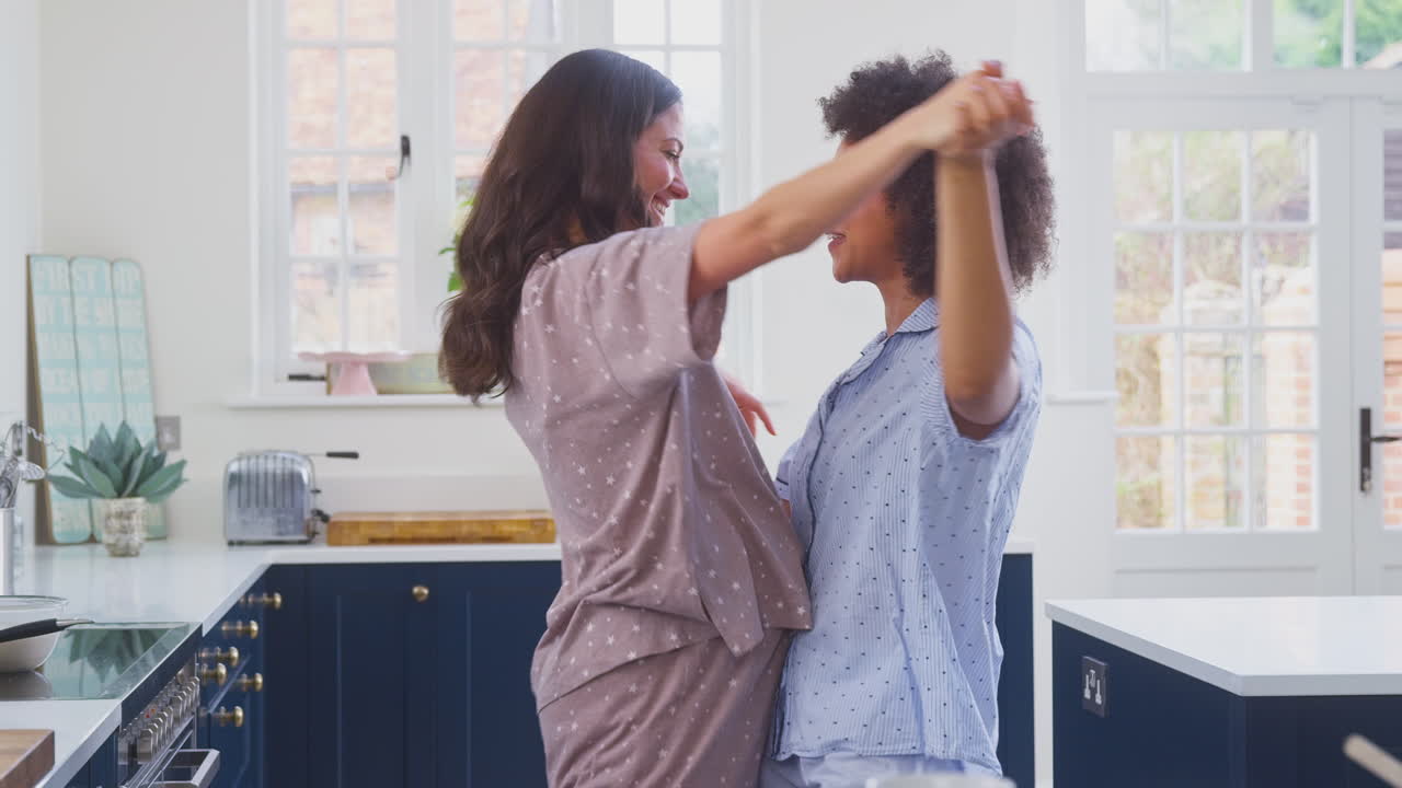 Pregnant Same Sex Couple Dancing Making Morning Pancakes In Kitchen