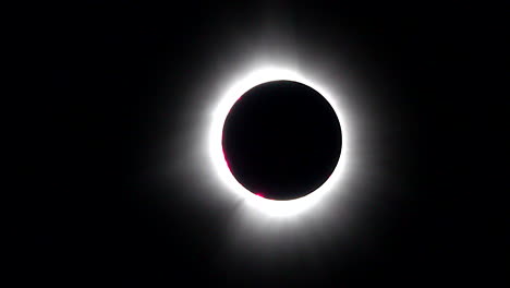 totality phase of total solar eclipse with bright red prominences and streaming corona