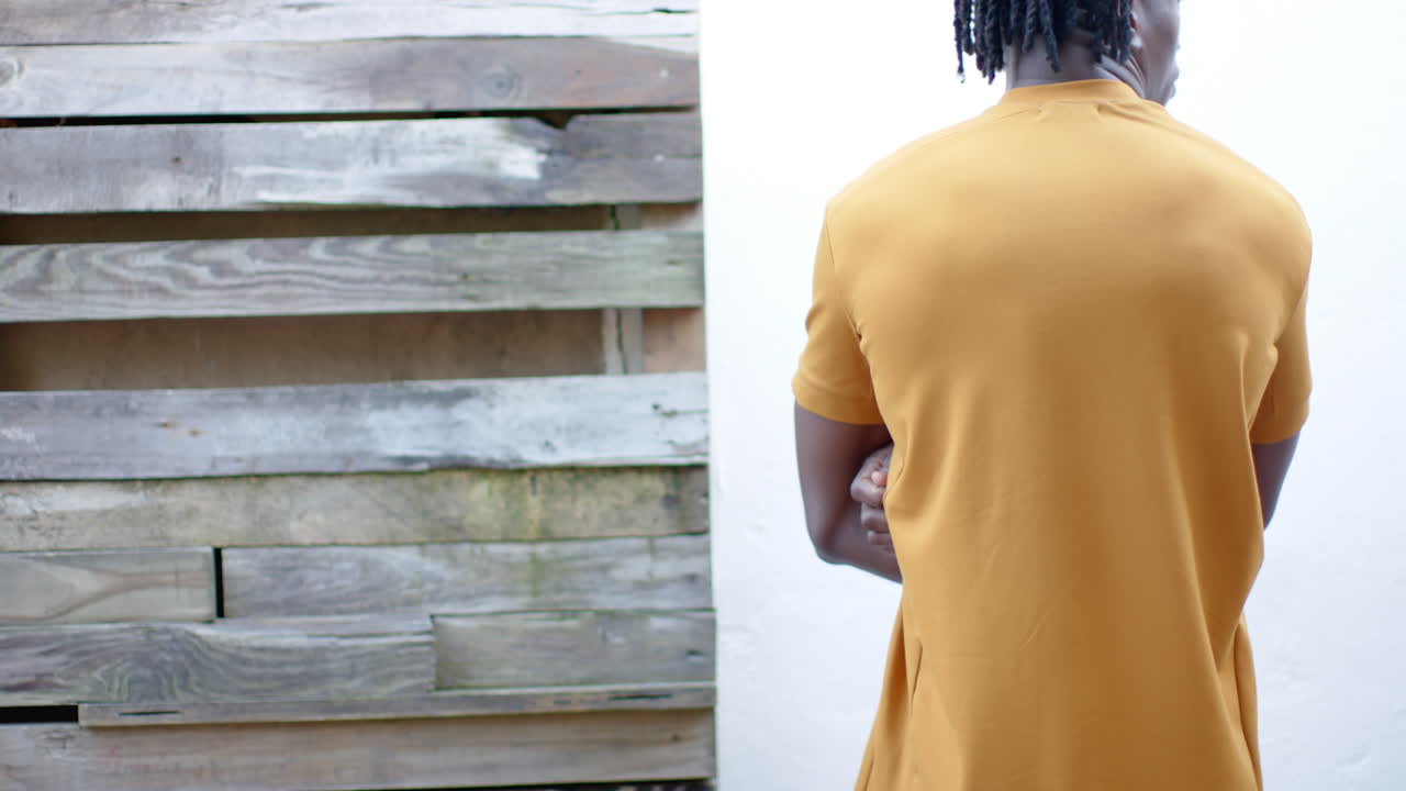 Rear view of african american man in yellow t shirt, with arms crossed, slow motion, copy space