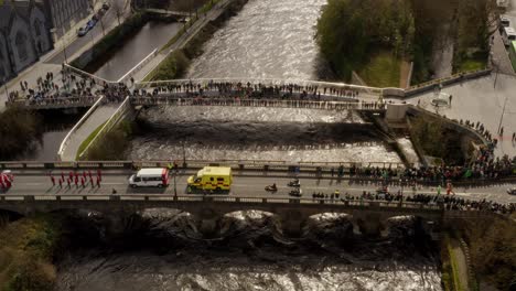 High-angle-aerial-view-above-Salmon-Weir-Bridge-as-ambulance-and-go-karts-line-up,-Galway-Ireland