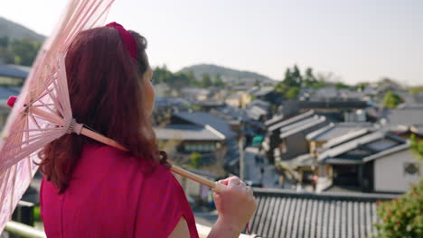 tourist with paper umbrella overlooking suburb from viewpoint in kyoto, japan