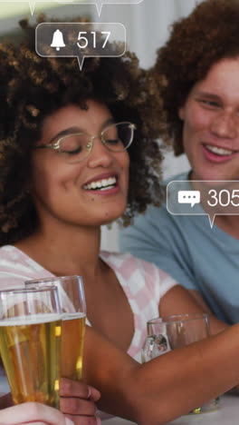 animation of media icons over happy diverse friends using smartphone with beer