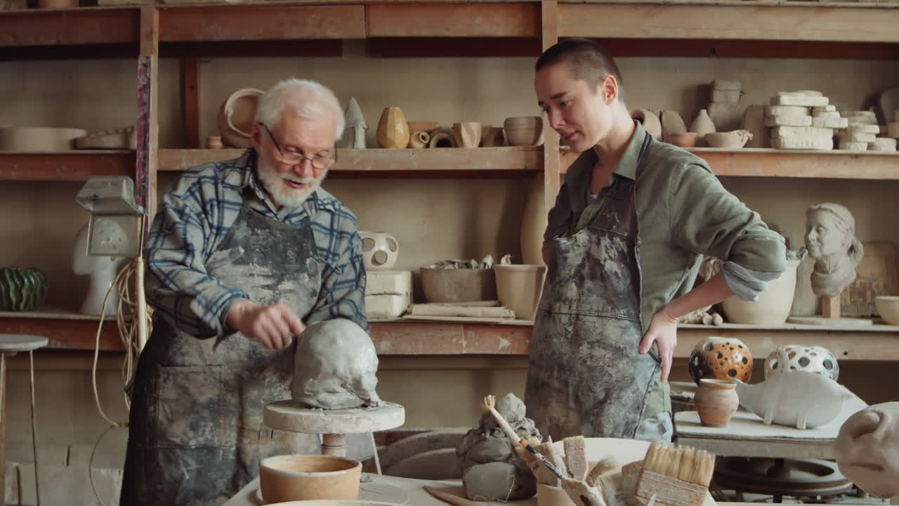 Senior Potter and Young Student Discussing a Sculpture