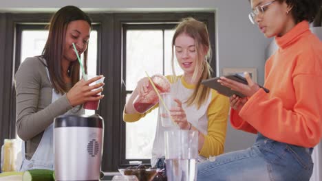 happy diverse teenager girls friends preparing healthy drink using tablet in kitchen, slow motion